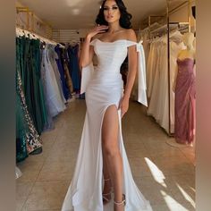 a woman in a white dress standing next to a rack of dresses and posing for the camera