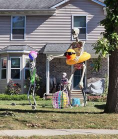 two skeleton statues in front of a house with balloons and decorations on the lawn outside