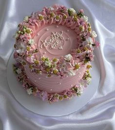 there is a pink cake with flowers on the top that says it's birthday