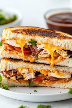 a grilled chicken and tomato sandwich on a white plate with some dipping sauce in the background