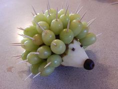 a hedgehog made out of grapes sitting on top of a counter next to an apple