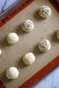 six balls of dough on a baking sheet with sprinkles and seasoning