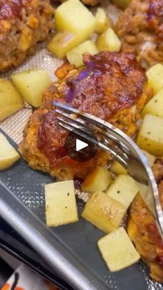 a fork is stuck into some food on a pan with potatoes and meatballs in it