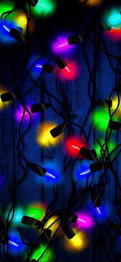 multicolored christmas lights are hanging on a wooden wall