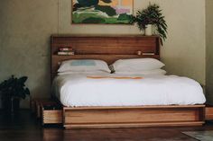 a bed with white sheets and pillows in a room next to a painting on the wall