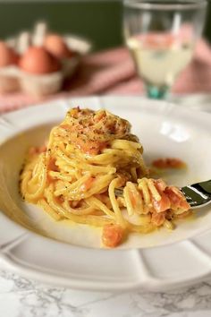 a white plate topped with pasta and meat covered in sauce next to a glass of wine