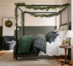 a canopy bed covered in christmas greenery and plaid blankets with pillows on the bottom