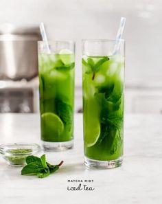 two tall glasses filled with green liquid and mint