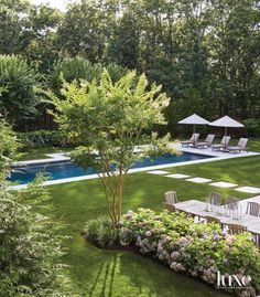 an outdoor pool surrounded by lush green grass and flowers with lounge chairs in the foreground