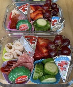 two plastic trays filled with fruit and veggies on top of a wooden table