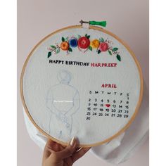 a person holding up a cross - stitch birthday card in front of a wall hanging