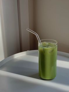 a green drink with a straw in it sitting on a white table next to a window