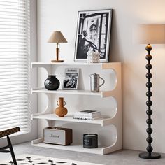 a white shelf with books and vases on it next to a lamp in a room