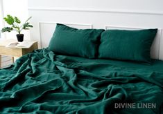 a bed with green sheets and pillows in a room next to a plant on a nightstand