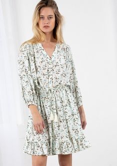 A style that is reminiscent of lazy Summer days and warm Summer nights. This charming ditsy floral mini dress features long voluminous sleeves with an elastic cuff, an adjustable tassel tie drawstring waist, and a flirty flounce-trimmed skirt. A timeless bohemian style. FINAL SALE Floral print Relaxed fit Long sleeve Elastic cuffs Mini length Flounce trimmed skirt V-neckline Banded collar Button front Tassel tie drawstring waist Model is 5'7, wearing a size S.Style: I-72374W-QZW-TC Spring Long Sleeve Dresses With Tassel Ties, Long Sleeve Bohemian Floral Dress For Daywear, Catching Fireflies, Lazy Summer Days, Small Floral Print, Band Collar, Ditsy Floral, Floral Mini Dress, Summer Nights