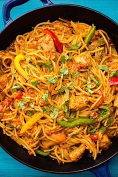 a skillet filled with noodles and meats on top of a blue wooden table