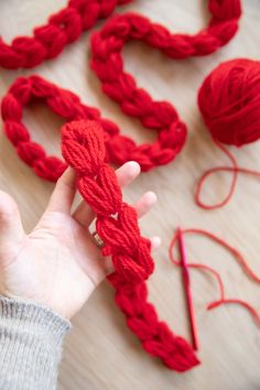 a hand holding a red rope with yarn next to it on top of a table