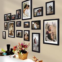 a bunch of pictures hanging on the side of a wall next to a vase with flowers