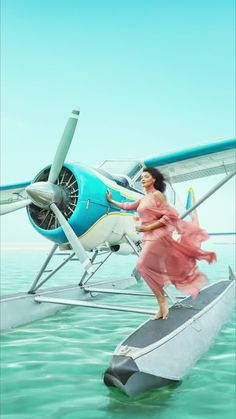 a woman in a pink dress is standing on the wing of an airplane over water