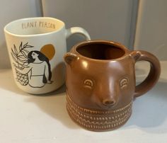 two coffee mugs sitting on top of a counter next to each other with faces painted on them