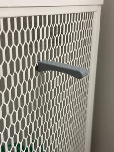 a close up of a metal door handle on a white mesh wall panel with green grass in the background