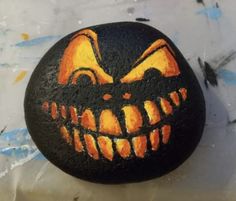 a painted rock with an evil pumpkin face on it's side, sitting on a table