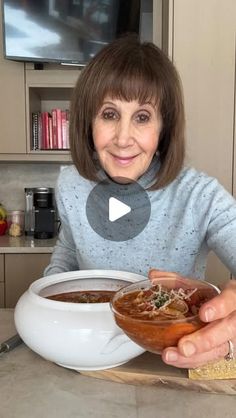 a woman sitting at a table holding a bowl of soup