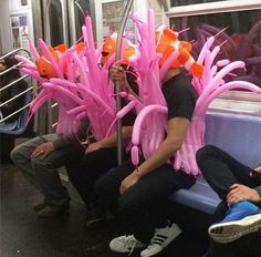 some people are sitting on a train with pink and orange balloons attached to their heads