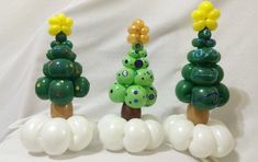 three green and yellow christmas trees on top of white balloons in front of a white backdrop