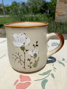 a coffee cup with white flowers painted on the side and brown rim sitting on a table