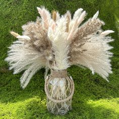 a vase filled with lots of white and brown feathers sitting on top of green grass