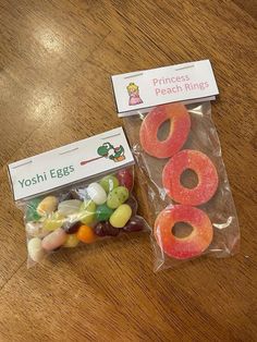 two bags of candy sitting on top of a wooden table next to an envelope with princess peach rings