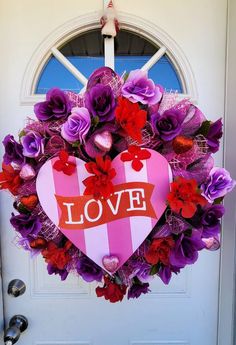 a heart shaped wreath with the word love written on it and purple flowers in front