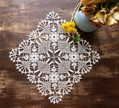 a white doily sitting on top of a wooden table next to a vase with flowers