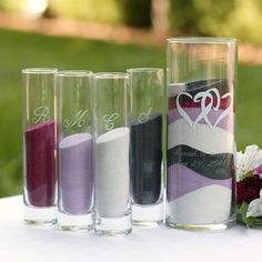 four different colored glasses sitting next to each other on a white tablecloth with flowers in the background