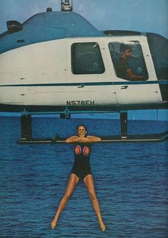 a woman in a black swimsuit standing on the water next to a helicopter with her legs spread out