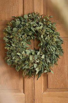 a wreath hanging on the front door of a house with green leaves and greenery