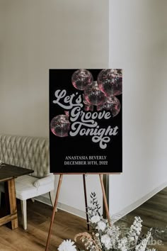 a black and white sign sitting on top of a wooden easel next to flowers