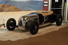 an antique race car is on display in front of a wall with a painting behind it