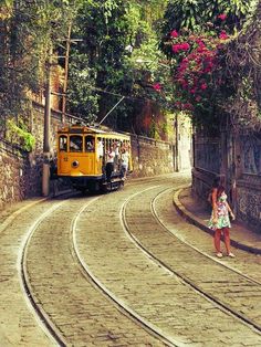 a woman standing on the side of a road next to a yellow trolley car with people in it