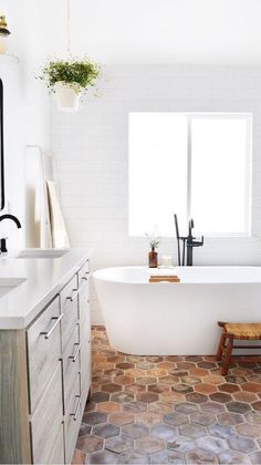 a white bath tub sitting in a bathroom next to a sink and window with potted plants