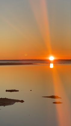 the sun is setting over water with rocks in it