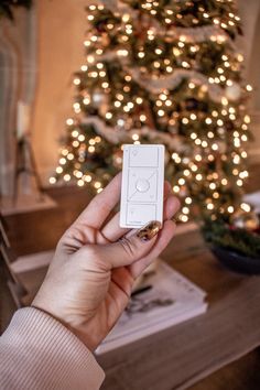 a person holding a wii remote in front of a christmas tree with lights on it