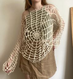 a woman standing in front of a white wall wearing a brown top with crochet on it