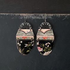 two oval shaped earrings with floral designs hanging from hooks on a black surface, next to each other