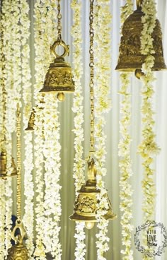 several bells hanging from the ceiling in front of white flowers and curtains with gold trimmings