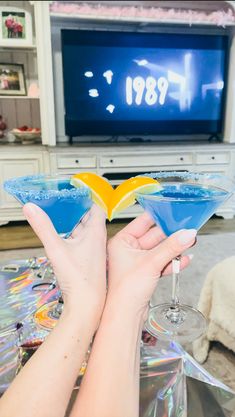 two people holding up martini glasses in front of a tv