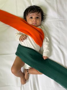 a small child laying on top of a bed with an orange scarf around it's neck