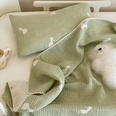 a small white animal laying on top of a bed under a green blanket next to a cup