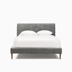 an upholstered bed with white pillows and grey linens on the headboard